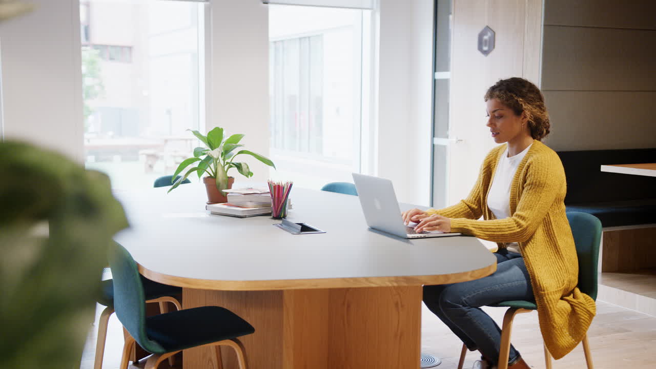 Young woman sitting at desk in an office using a laptop computer, slow motion