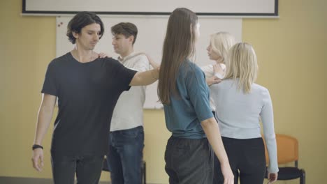 grupo de actores profesionales que entrenan habilidades en el interior. hombres y mujeres caucásicos confiados que se sostienen los hombros con las manos y caminan en círculo. jugando a un juego para la educación en artes escénicas