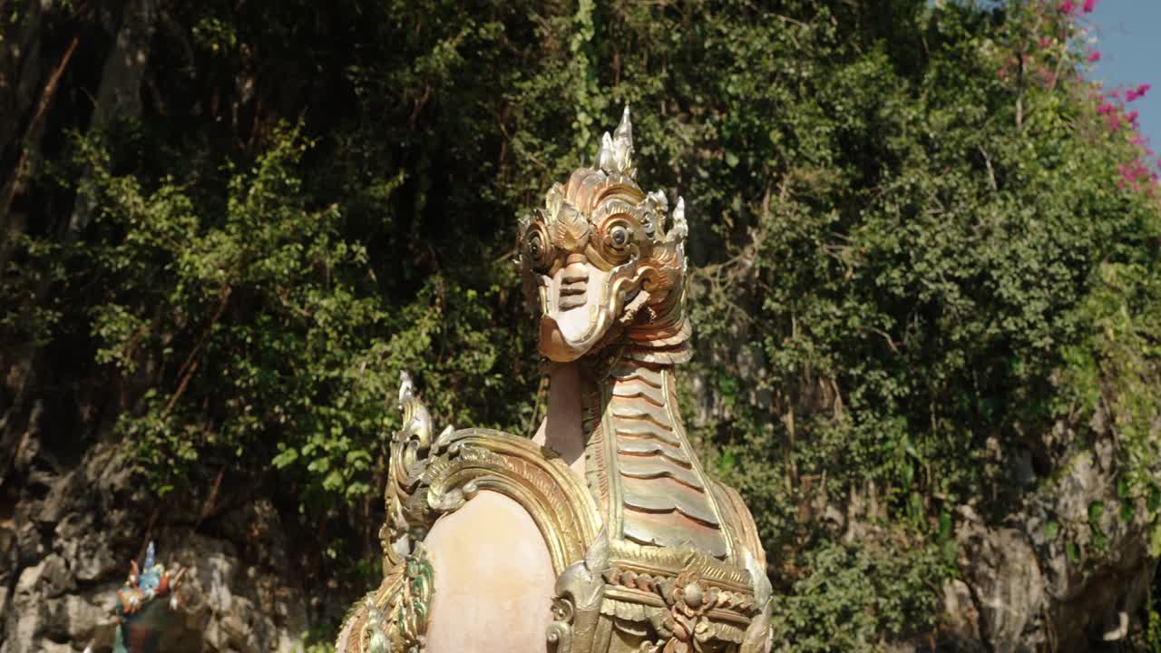 A detailed mythical guardian statue glows under sunlight against lush greenery at Wat Tham Phra, Thailand