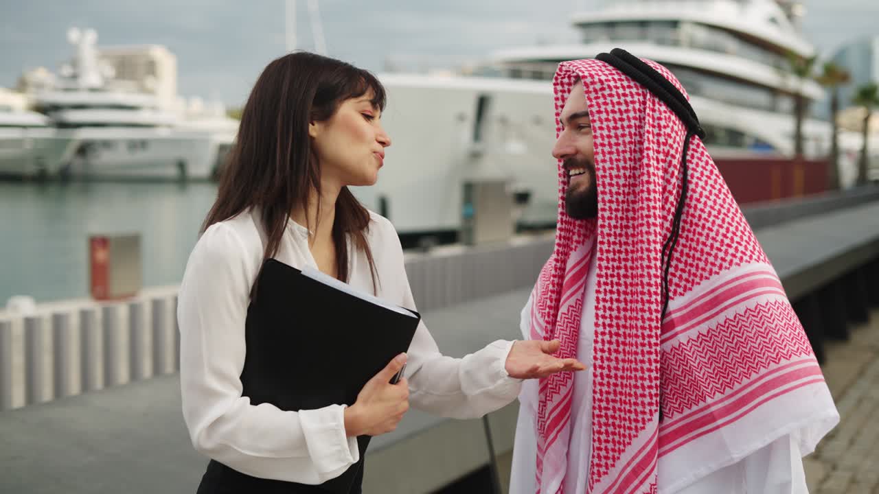 un empresario saudí sonriente hablando con una agente de yates profesional antes de comprar un barco en el puerto