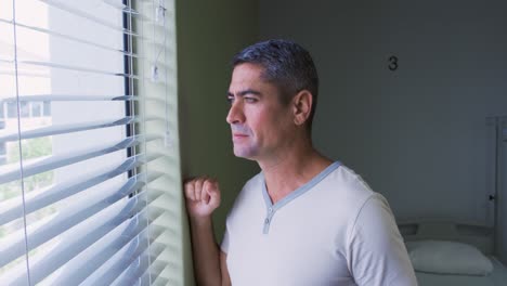 Side-view-of-Caucasian-male-patient-standing-near-window-in-the-hospital-ward-4k