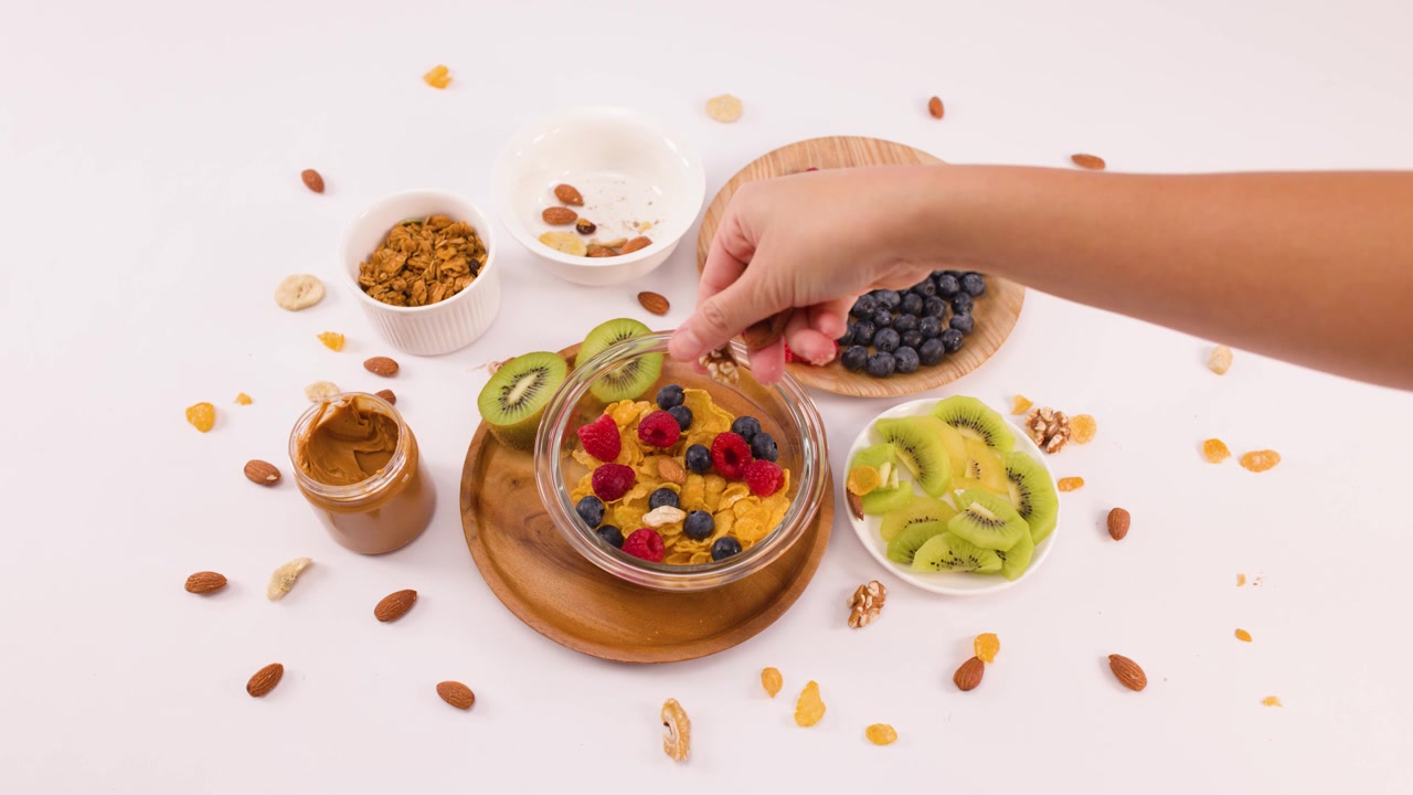 Toma aérea de una mano esparciendo nueces en un tazón de cereal con bayas y kiwi