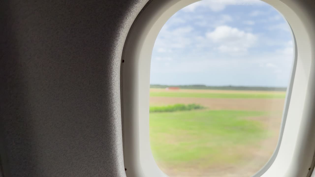 Airplane window view of green fields and blue sky, smooth camera movement, natural daylight