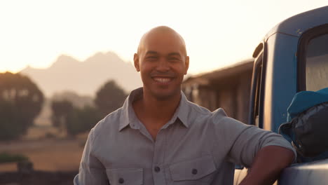 Portrait-Of-Man-Standing-Next-To-Pick-Up-Truck-On-Road-Trip-To-Cabin-In-Countryside