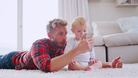 Dad-lying-on-floor-at-home-taking-selfies-with-toddler-son