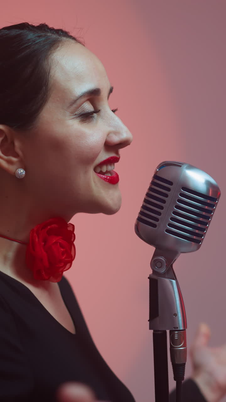 Close-up of a passionate female singer with red lips and a red ribbon on her neck, singing into a vintage microphone, as she moves her hands expressively,camera slowly zooming out