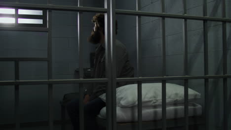 el criminal se sienta en la cama en la celda de la prisión mira a la ventana cerrada