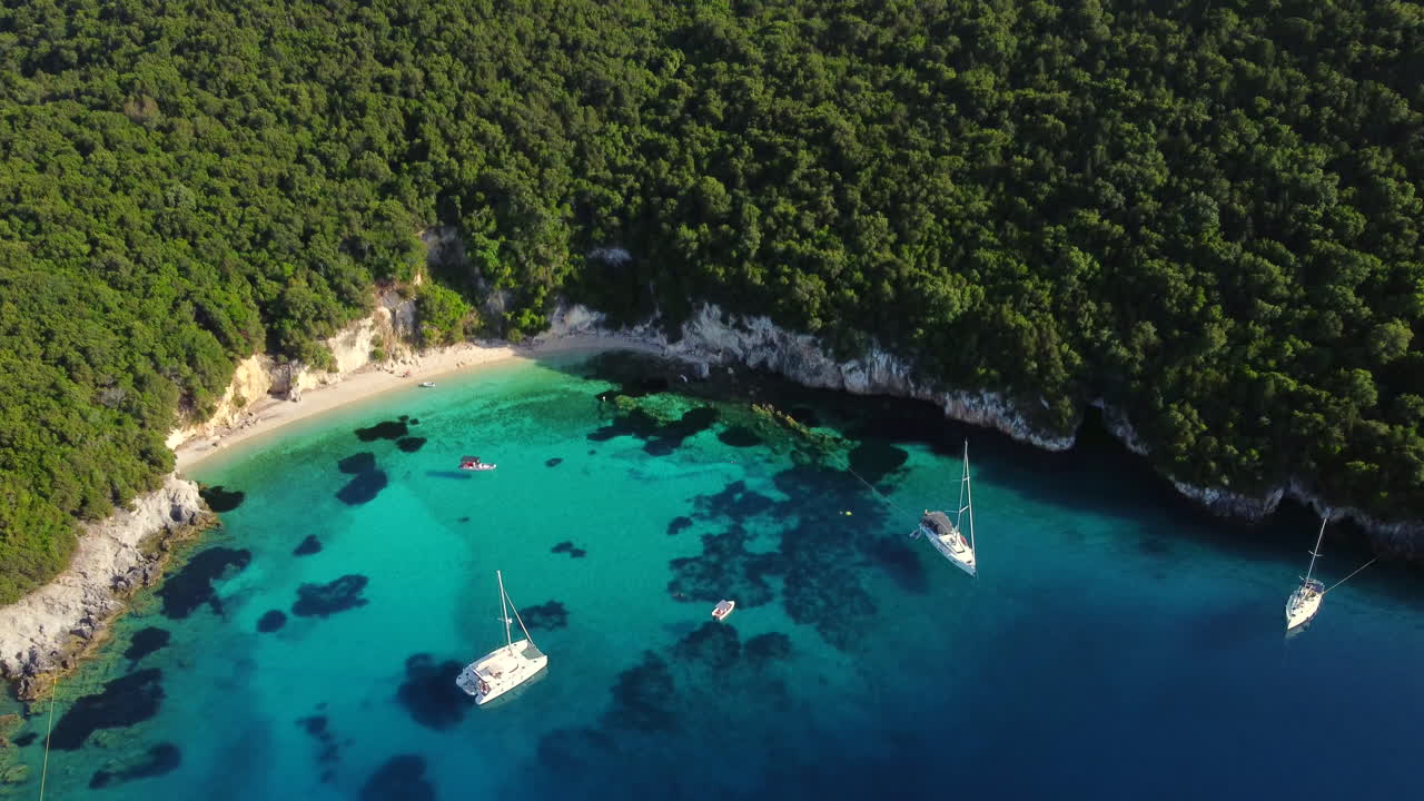 Inclinazione aerea verso il basso sulla iconica spiaggia della Laguna Blu, Sivota, Grecia, yacht di lusso sul cristallino Mar Ionio turchese