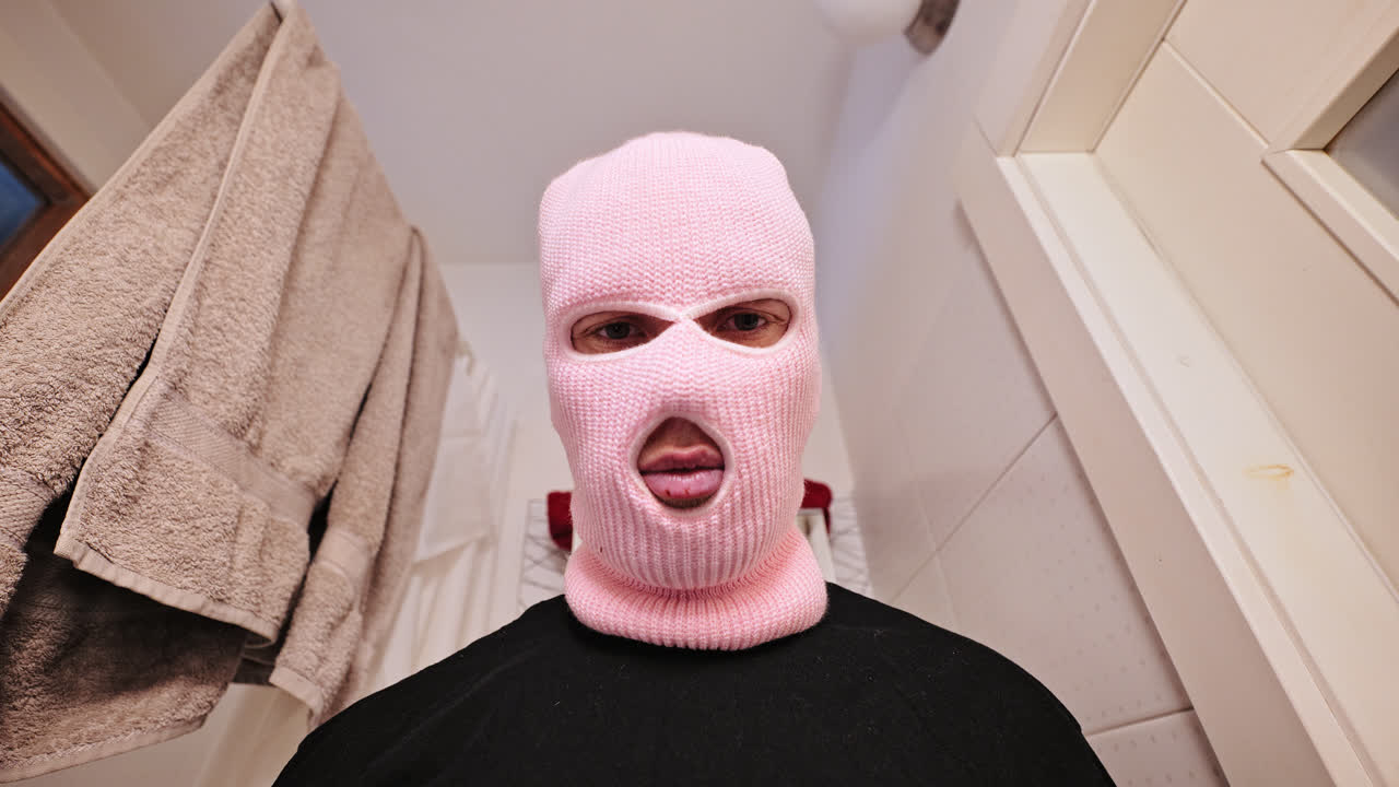 Knitted pink balaclava mask and intense expression, tight space Soviet bathroom