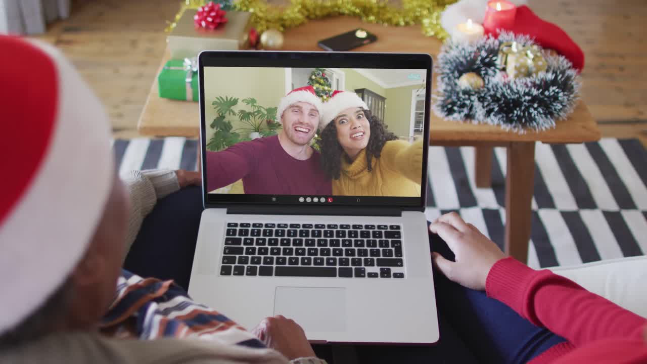 madre y hija afroamericanas usando una computadora portátil para una videollamada de navidad con la pareja en la pantalla