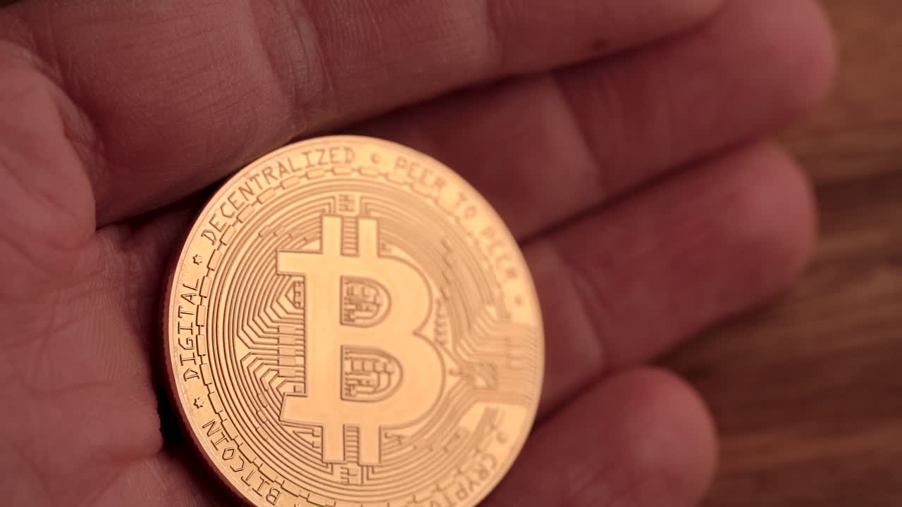 un bitcoin dorado sostenido en una mano muy cerca y movido lentamente