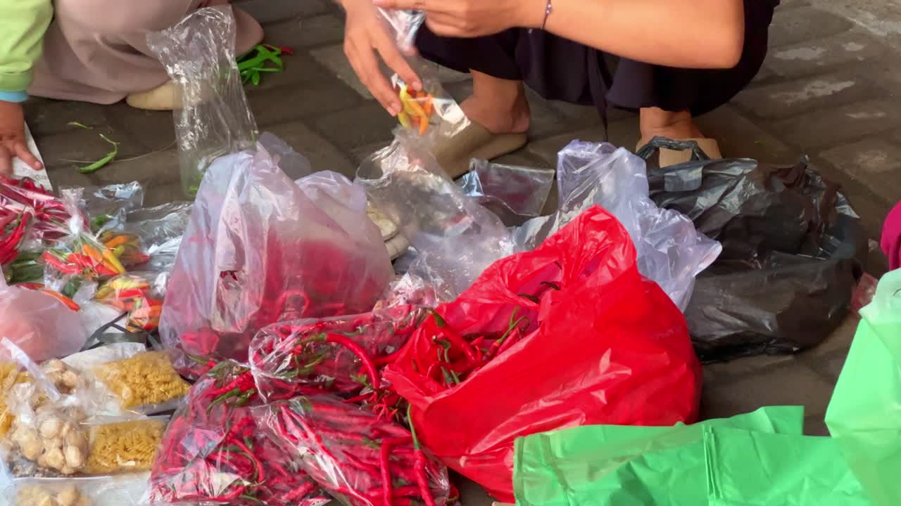 Hands sorting and packing chili peppers into plastic bags. Street market food preparation and fresh produce handling