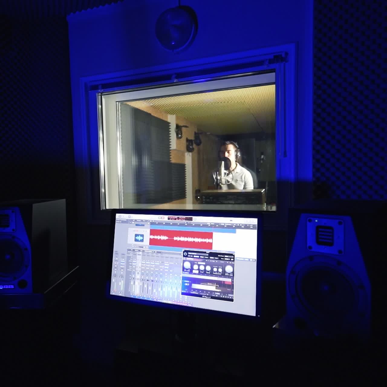 Dark room with modern equipment for music recording. Male singer stands in front of microphone performing a song