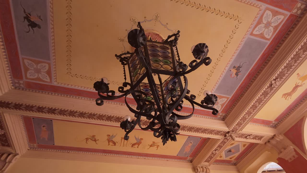 Entrance hall of a historic building in Orta San Giulio, Italy. Ornate chandelier, vibrant frescoes, and classic tiled flooring create an inviting atmosphere in this charming Italian location