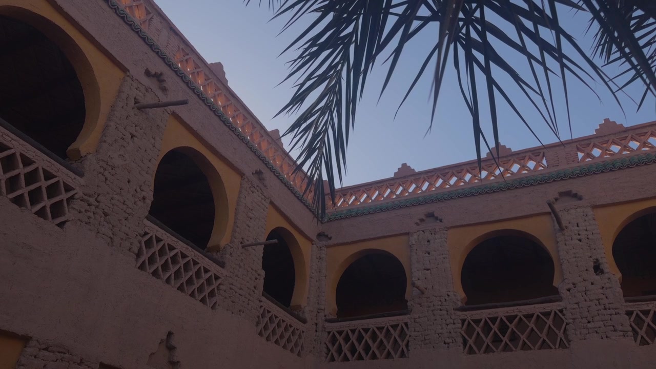 Vista dal basso di balconi ad arco ornati e ringhiere a graticcio di un riad marocchino con fronde di palma.