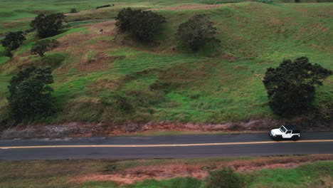 Toma-De-Seguimiento-De-Jeep-Blanco-Conduciendo-En-Una-Carretera-Escénica-Con-Paisaje-Verde---Vista-Aérea