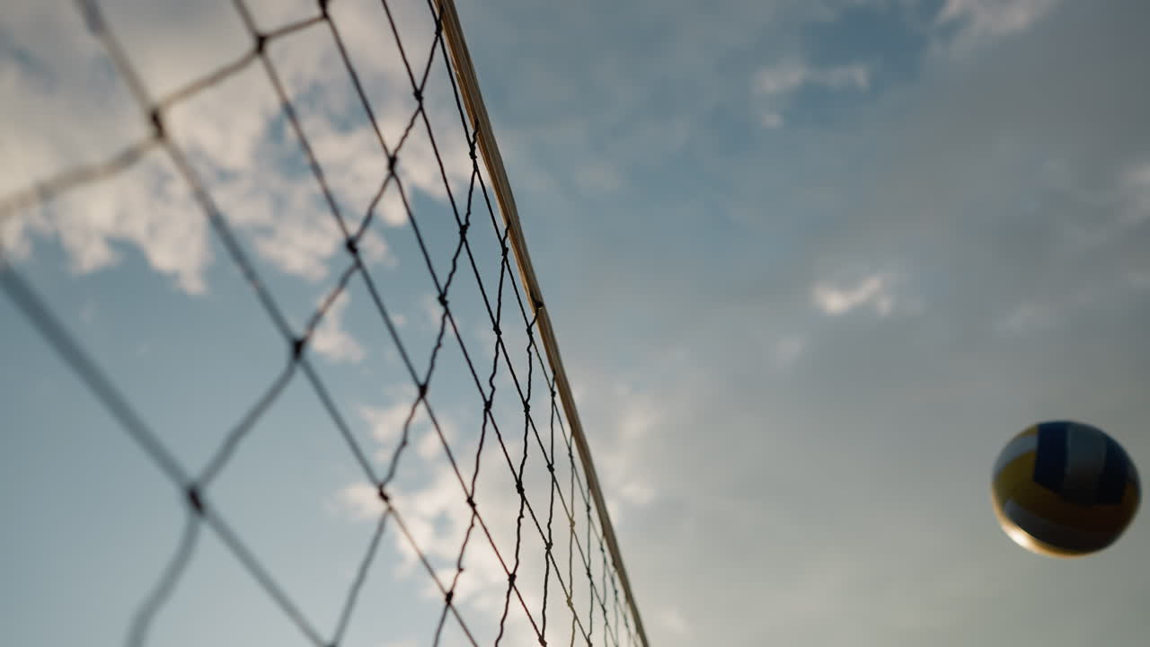 Primo piano di una rete da pallavolo con una palla giocata sopra, sullo sfondo del cielo, che mostra l'azione in una partita di pallavolo all'aperto con cielo sereno e luce solare intensa
