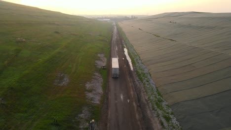 truck hauling garbage in a landfill from canada to michigan, usa, aerial drone view during bright sunrise