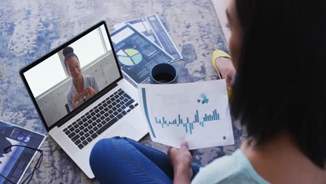 African american woman holding a document having a video call with female colleague on laptop