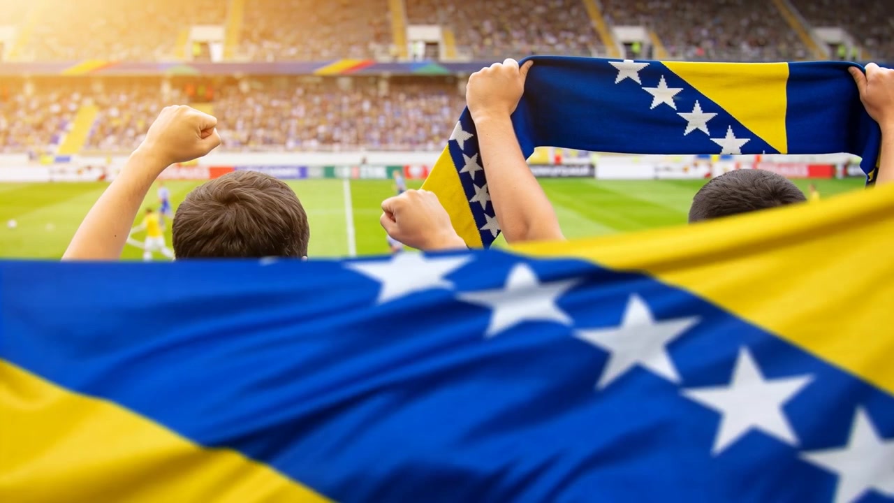 No pontapé inicial, dois torcedores com camisas do time segurando um cachecol, apoiando a equipe nas arquibancadas, com a bandeira da Bósnia tremulando.