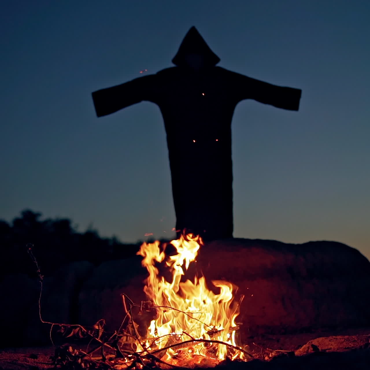 Scary dark figure with hood waving arms. Bonfire burning and mysterious ghost in black costume outdoors. Halloween costume.