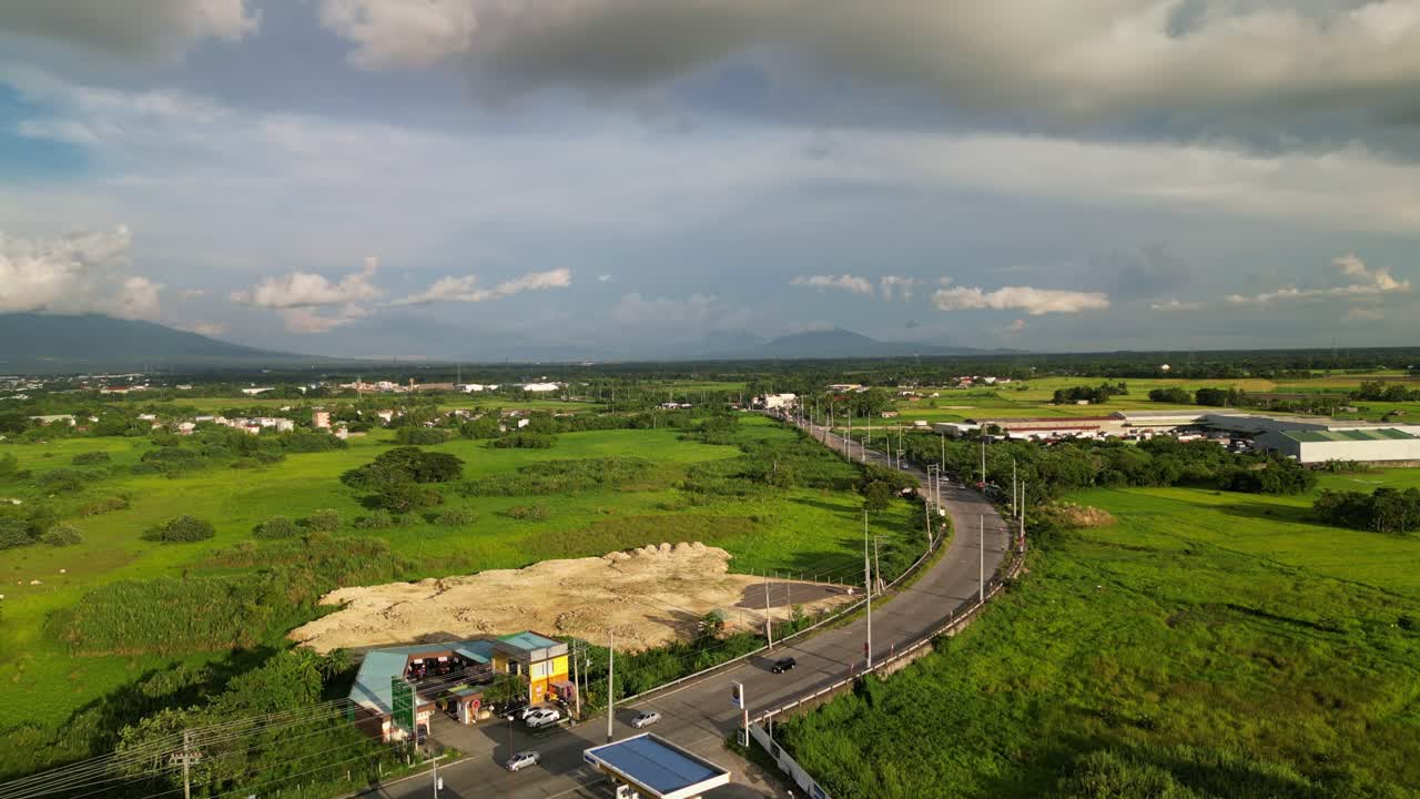 Vibrant aerial drone shot of curved, provincial highway road along lush green fields and cloudy skies at Bicol Region, Philippines