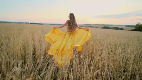 woman in yellow dress running through a wheat field at sunset