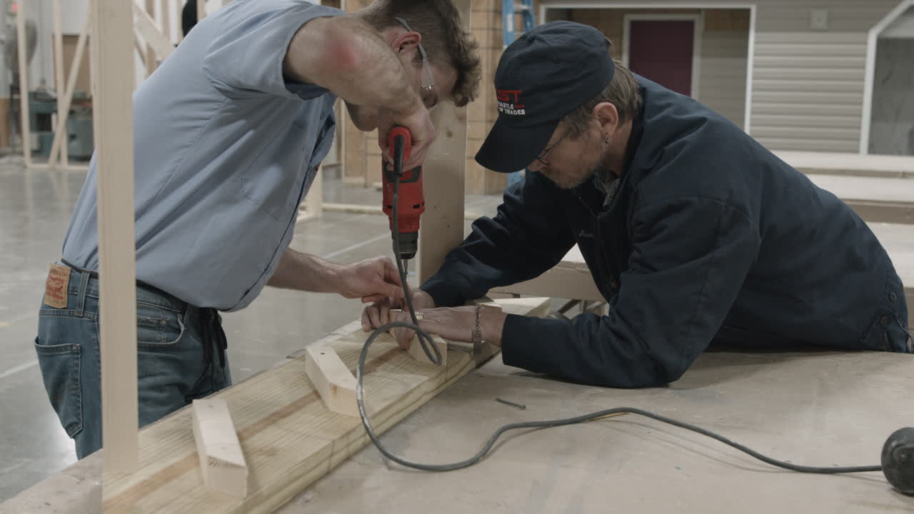 Trade school carpentry workshop instructor assists student with building a staircase