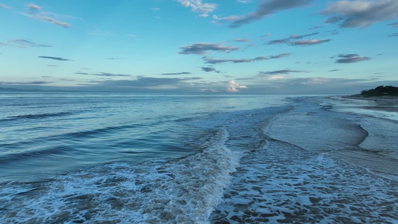 뒤로 날아가는 모래 해변과 푸른 물결 모양의 물과 함께 석양의 골드 코스트 해변에서 파도의 매우 낮은 각도 샷