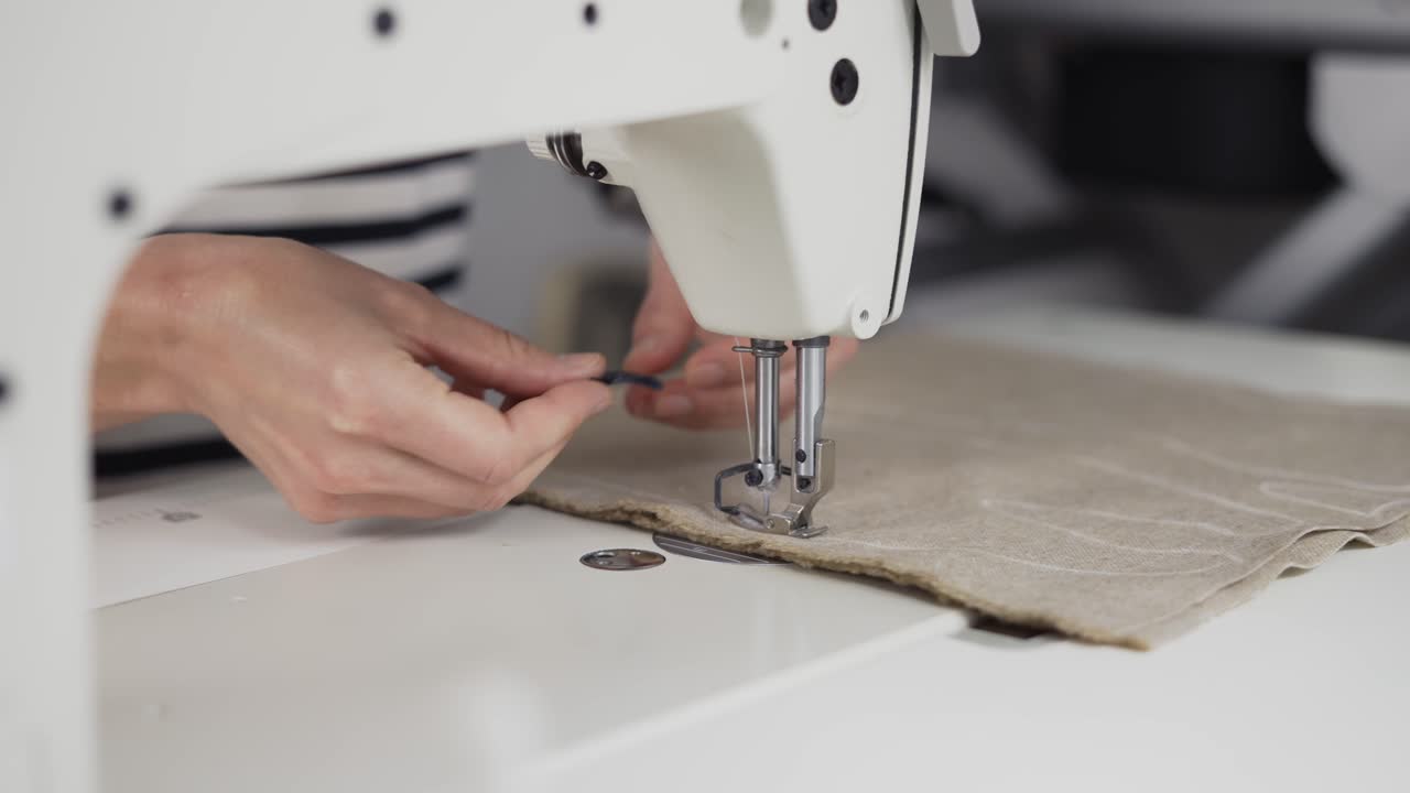Closeup of a young woman's hands sewing beige fabric with a sewing machine