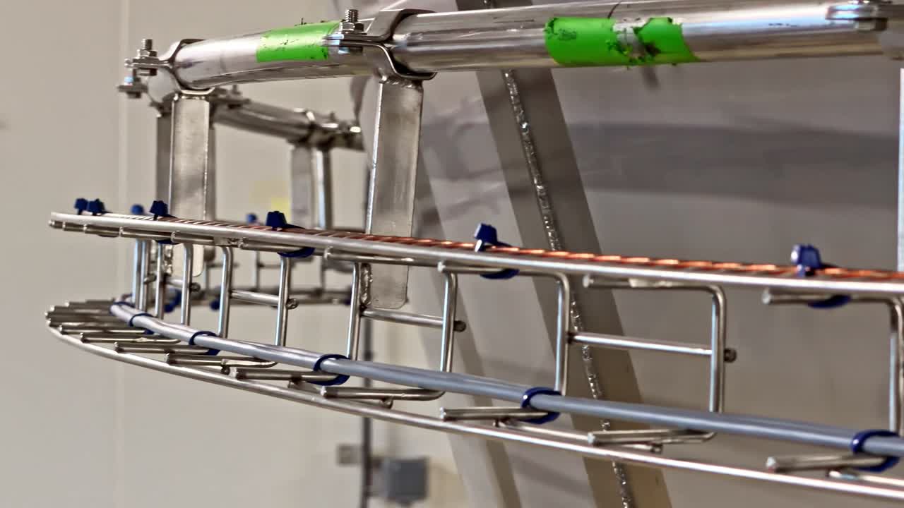 Stainless steel industrial cable tray and tubing system inside a modern factory, showing clean infrastructure for automation, utilities, and process equipment