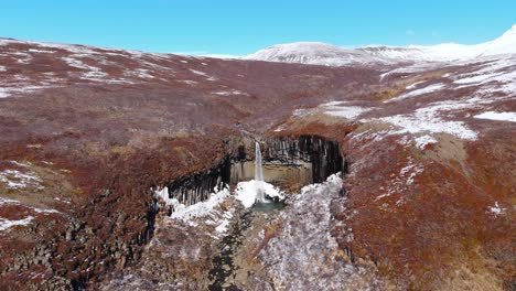 Formaciones-Volcánicas-De-Color-Marrón-Terroso-Alrededor-De-La-Cascada-De-Svartifoss-Columna-De-Basalto-Drone