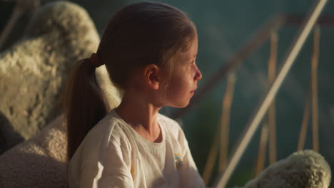 kid looks out of transparent wall of tent. calm child looks into distance dreamily resting in glamping at dawn. happy kid sits in comfortable chair