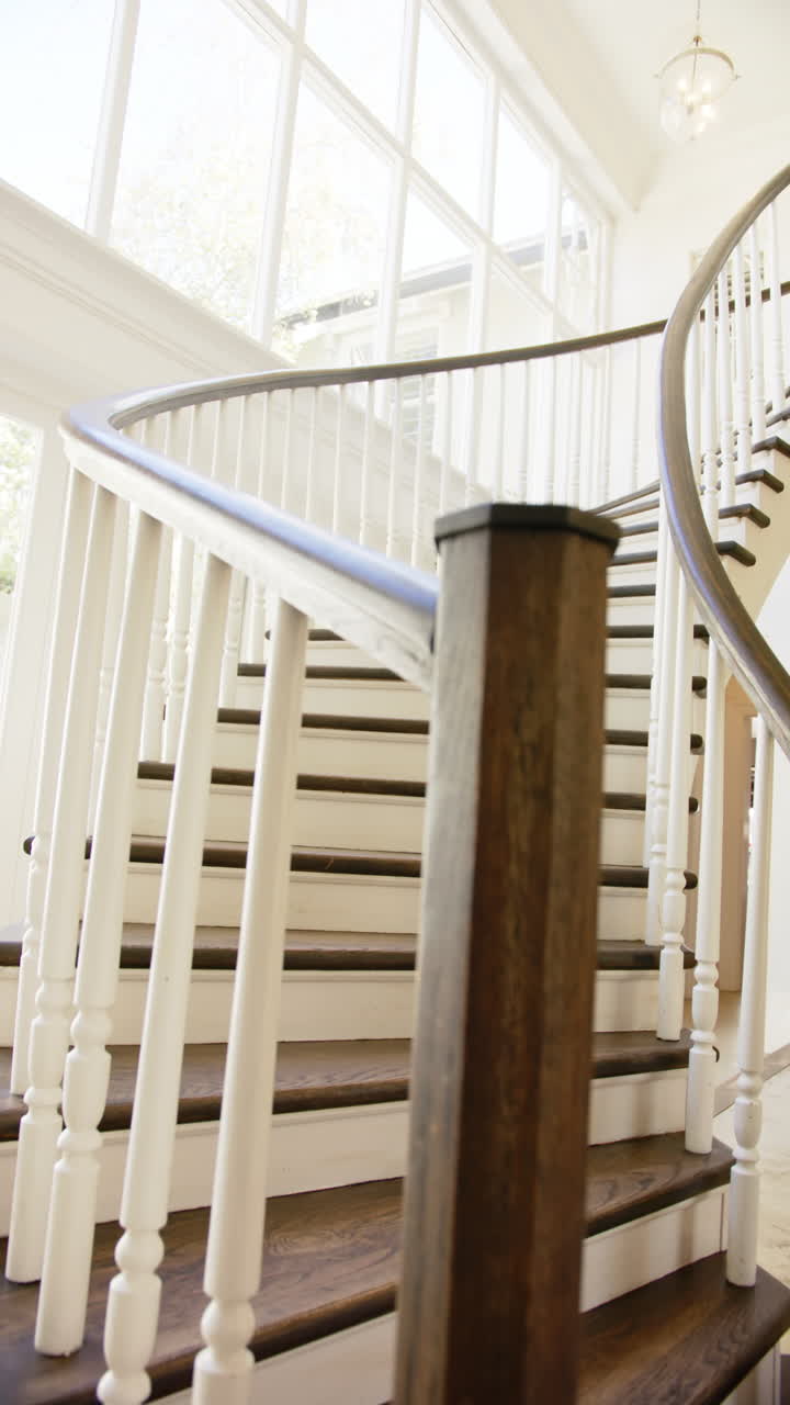 Video verticale: Scala curva con corrimano in legno in un interno di casa moderno e luminoso.