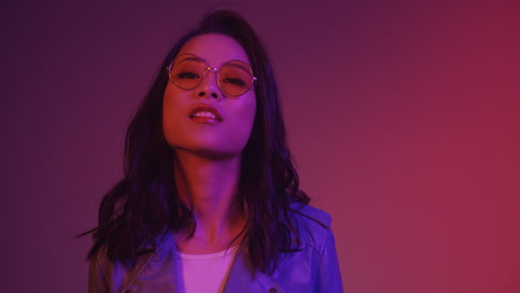 close up of young woman in sunglasses looking at camera while standing on pink neon background