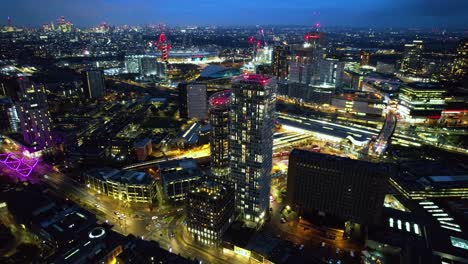 Stratford-Futurista-Iluminado-Por-La-Noche-De-Lujo-En-El-Centro-De-Edificios-De-Gran-Altura-Vista-Aérea-Dolly-Derecho