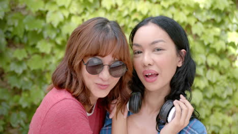 Two-young-biracial-female-friends-are-laughing-together,-one-wearing-sunglasses-and-headphones