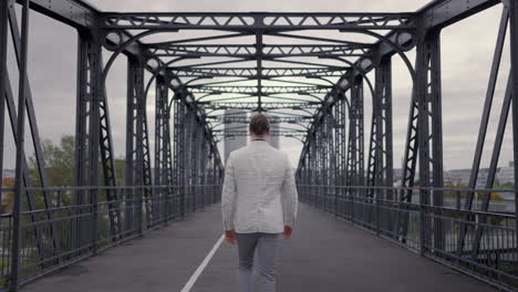 confident adult businessman in formal suit walking through the bridge at the morning