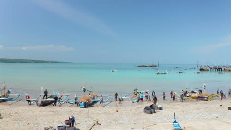 Pescadores-En-Coloridos-Barcos-Tradicionales-En-La-Playa-De-Arena-En-Bali,-Indonesia.-Pescadores-De-Vista-Aérea-Sacando-Peces-De-Las-Redes-De-Pesca-En-Canoas-Jukung-En-La-Playa-De-Arena-Tropical