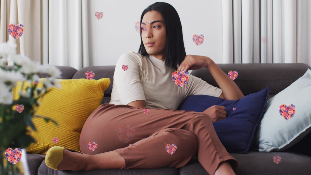 animación de iconos de corazón con flores sobre mujer biracial sentada en el sofá