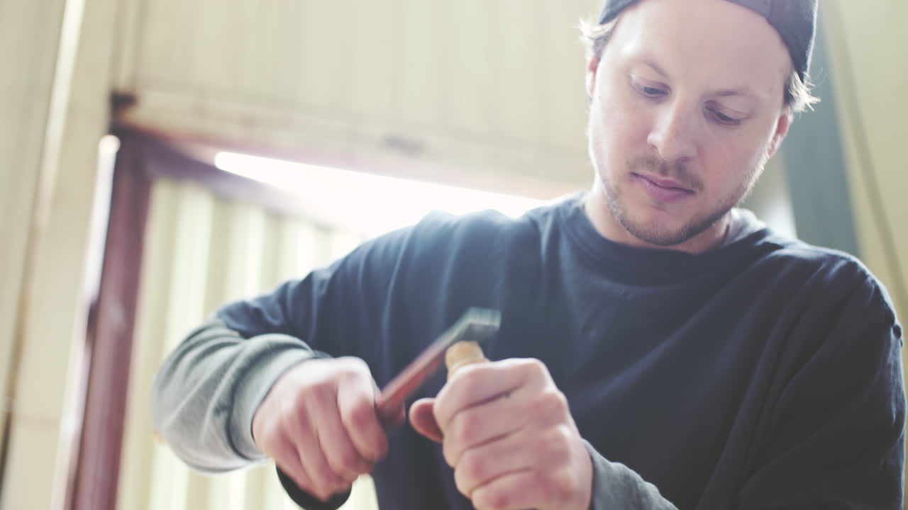 Man Carving Wood with Chisel and Hammer in Workshop
