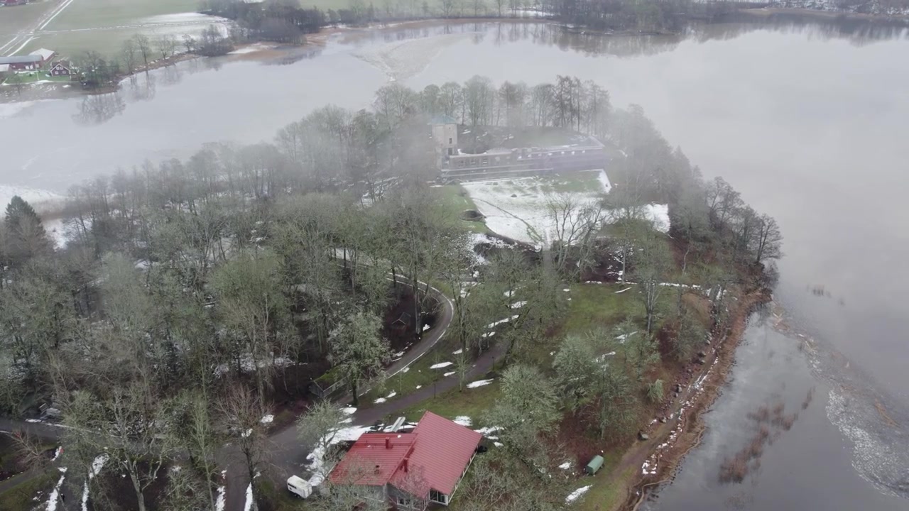 Ripresa aerea con drone che mostra il Parco del Castello di Grafsnas accanto al Lago Anten con terreno innevato, alberi spogli, nebbia e acqua invernale a Sollebrunn, Alingsas, Svezia, durante il giorno