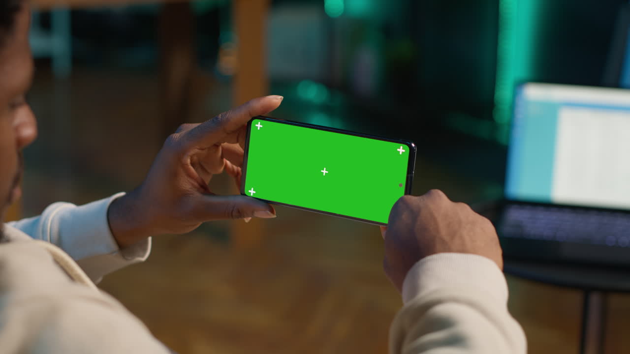 African american person using device with green screen from the comfort of his modern trendy home, sitting on the couch and working in the living room. Happy confident young man. Camera A.