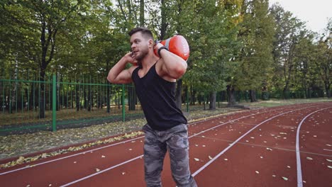 male bodybuilder having his workout outdoors. handsome athlete lifting 10 kg weights on the stadium. slow motion.