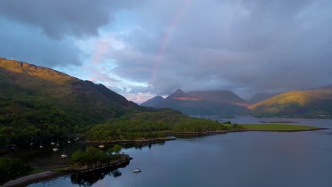 4k aerial drone footage of a rainbow in a cloudy sky with sailboats on the water in the scottish highlands scotland at sunset