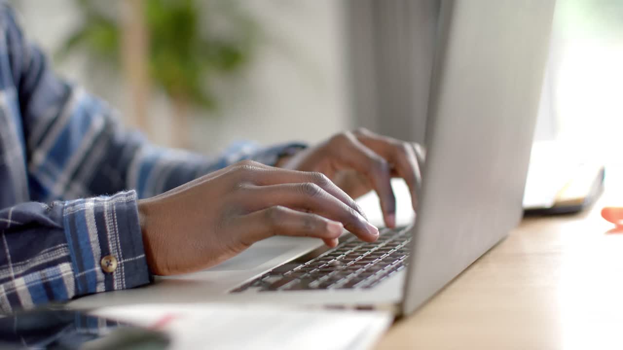 sección media de un hombre afroamericano sentado en la mesa usando una computadora portátil en casa, en cámara lenta