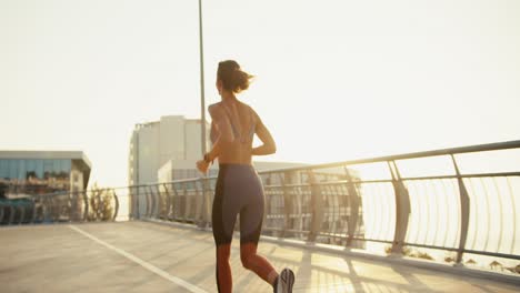 Vista-Trasera-De-Una-Joven-Atlética-Con-Uniforme-Deportivo-De-Verano-Corriendo-Por-La-Mañana.-Rayos-De-Sol-Del-Amanecer