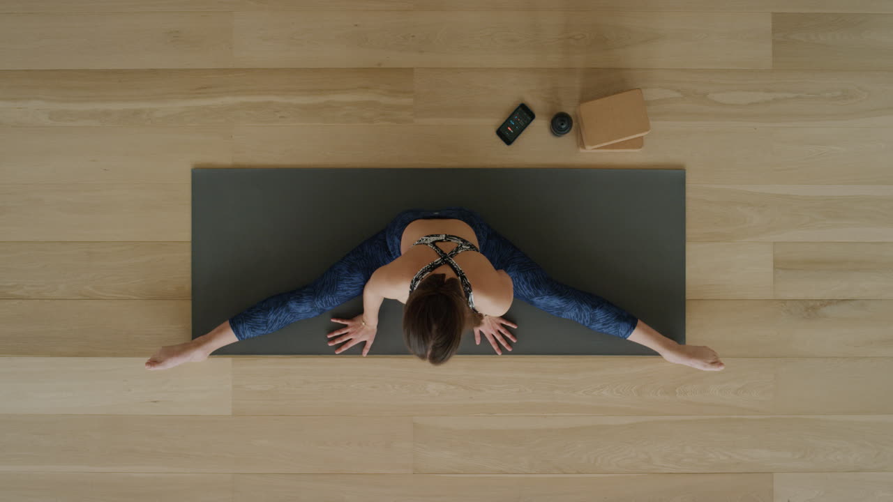 vista superior de una mujer de yoga practicando una pose de gran angular sentada de lado en un estudio de ejercicios disfrutando de un estilo de vida saludable practicando meditación en una colchoneta de ejercicios