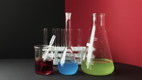 Coloured-liquids-in-flasks-with-test-tubes-in-stand-on-black-and-red-background,-slow-motion
