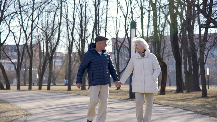 Senior couple holding hands, walking and laughing in the park on a winter day